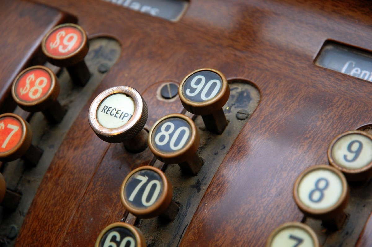 Close-up of the brass keys on an old cash register, stamped with dollar and cent values next to a worn receipt button.