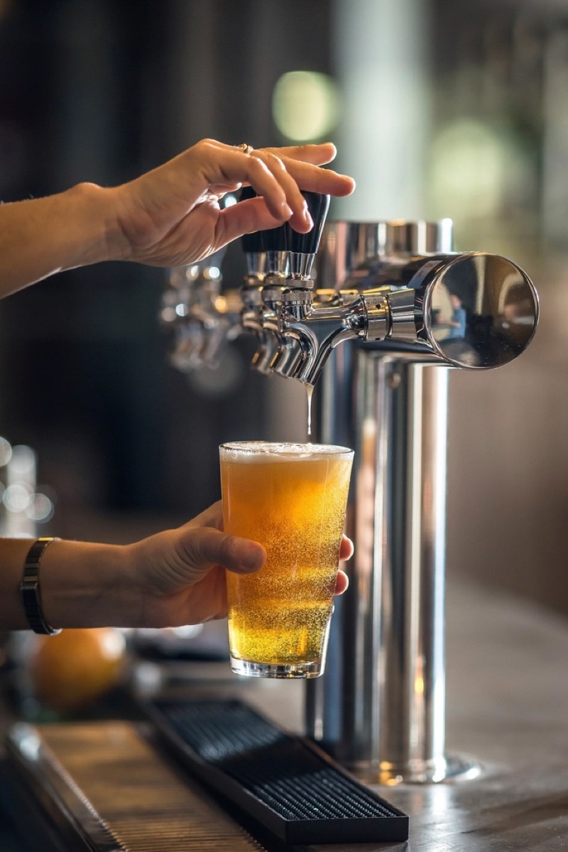 Bartender pouring a beer from a chrome tap into a pint glass at a bar