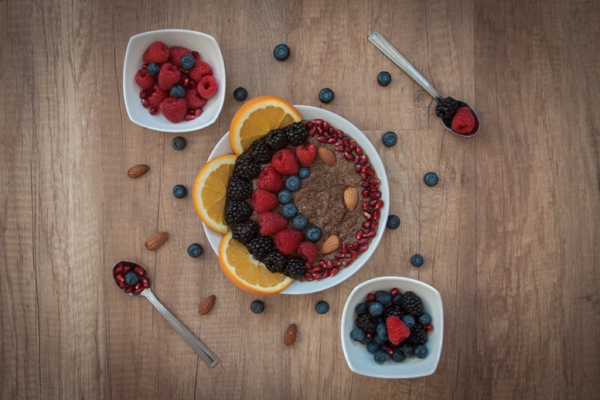 An overhead breakfast bowl topped with blackberries, raspberries, blueberries, orange slices and almonds