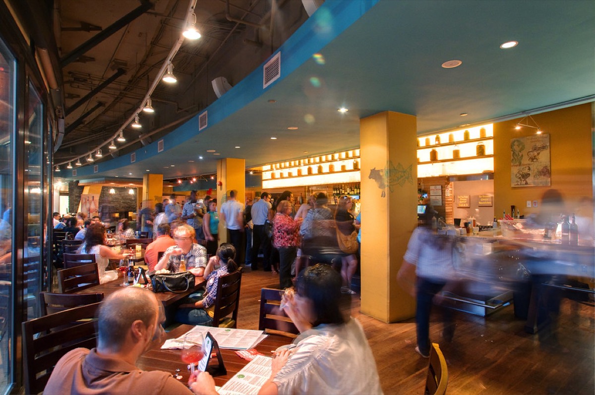 A lively restaurant and bar packed with seated diners and standing patrons under warm lighting