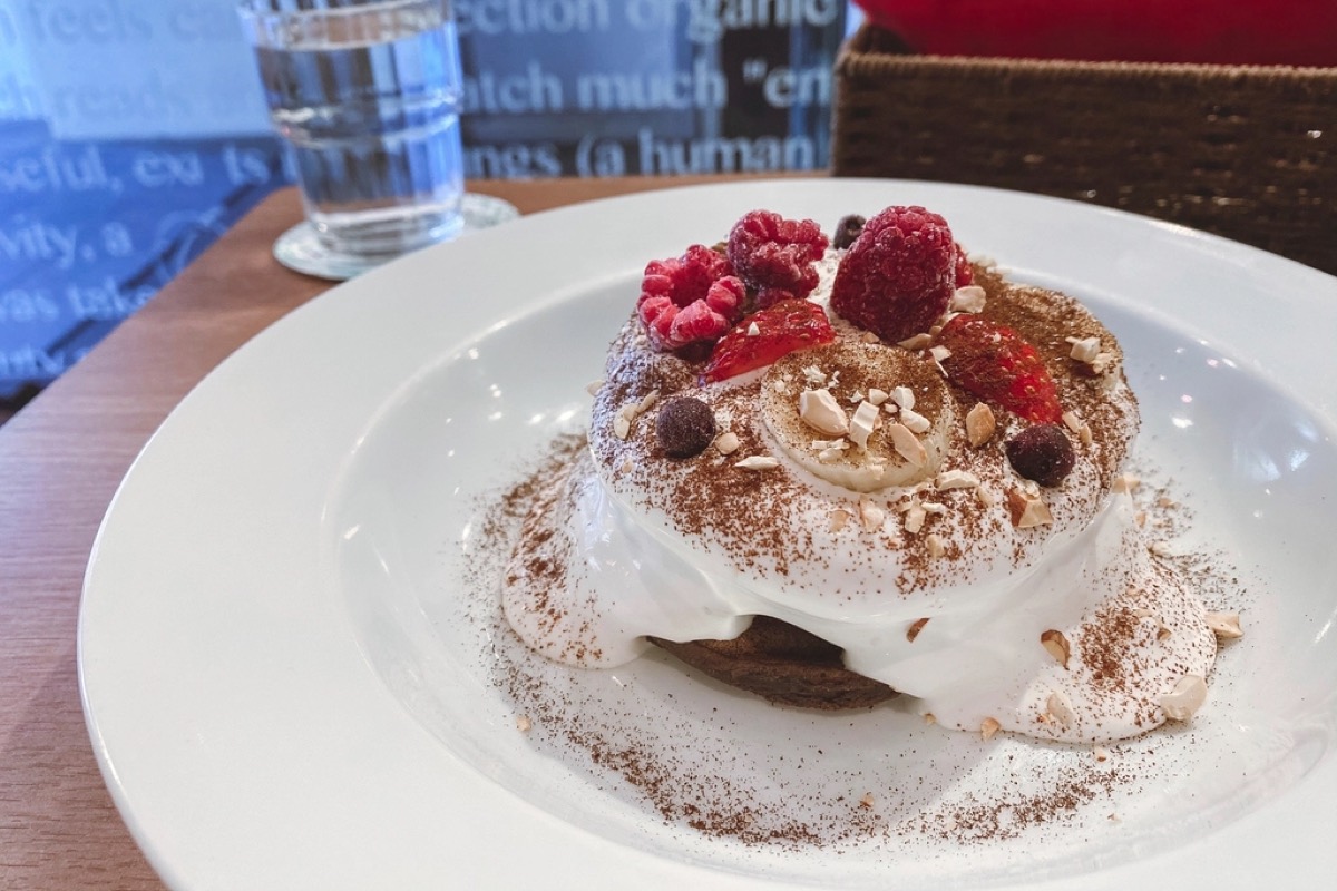 A cafe dessert stack topped with whipped cream, raspberries, banana, cocoa dust and chopped nuts