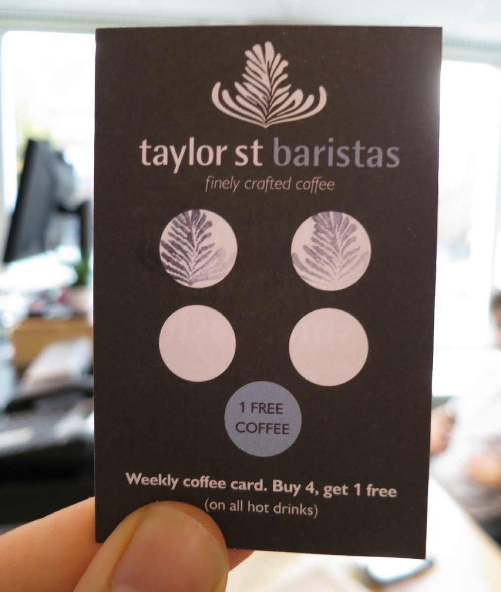 A hand holding a dark brown cafe loyalty stamp card with two coffee leaf stamps filled in and a free coffee circle at the bottom