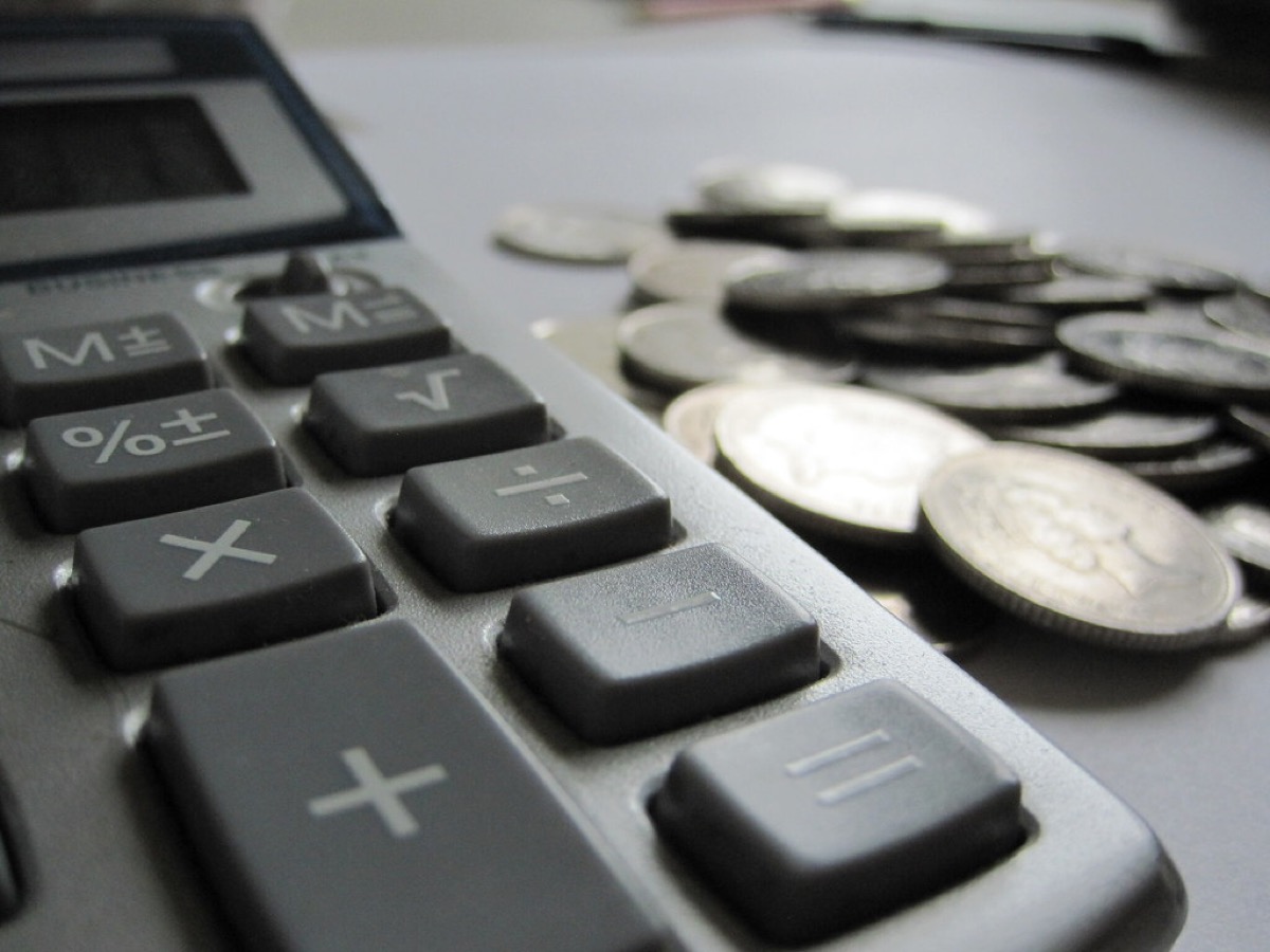 Close-up of a calculator's plus, minus, multiply and divide keys next to a small pile of loose coins on a desk.
