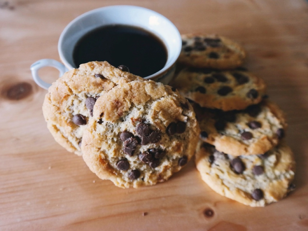 Freshly baked chocolate chip cookies fanned out beside a cup of black coffee on a wooden table