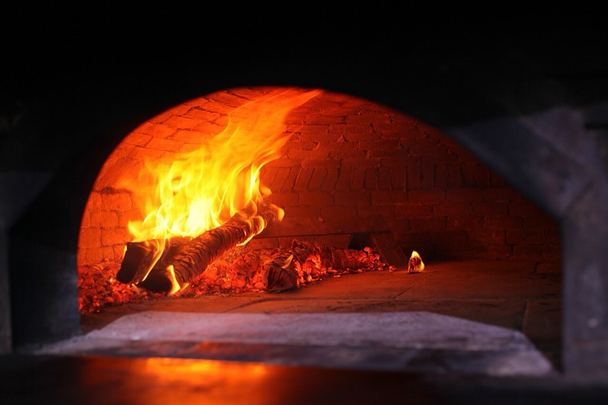 Burning wood and glowing embers inside the brick chamber of a commercial wood fired oven