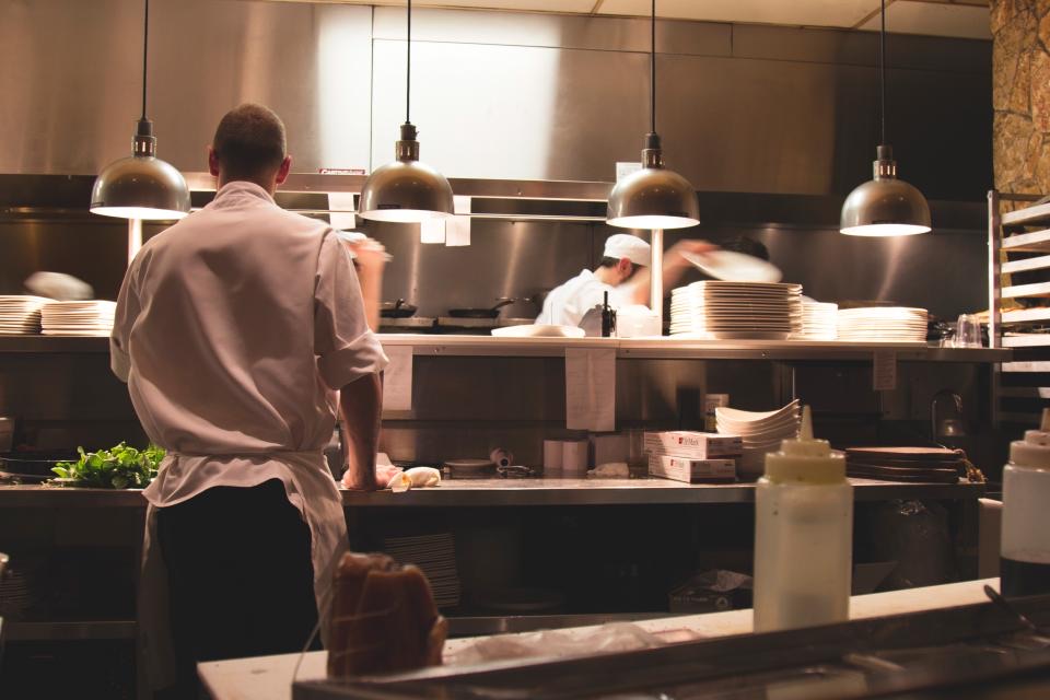 Chefs plating food under pendant lights in a professional stainless steel restaurant kitchen