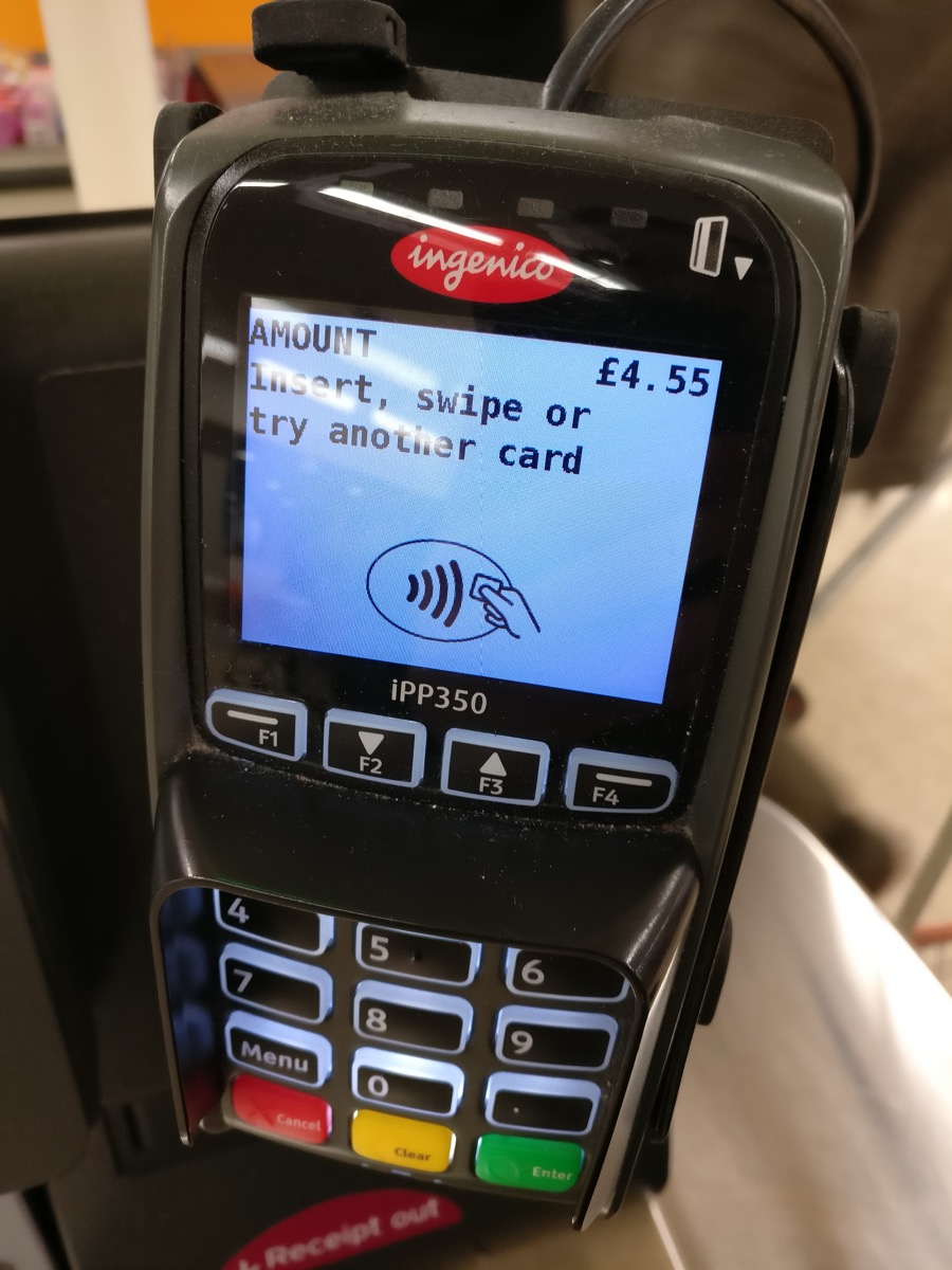 A countertop card payment terminal displaying an amount and the contactless tap payment symbol