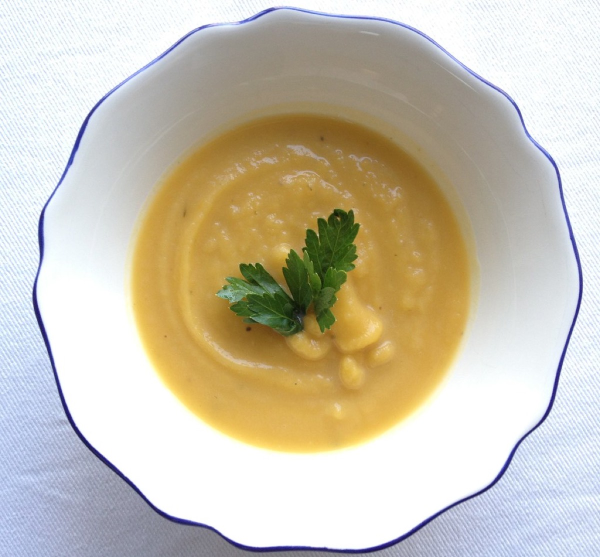 An overhead bowl of smooth pumpkin soup garnished with a sprig of parsley in a blue-rimmed bowl