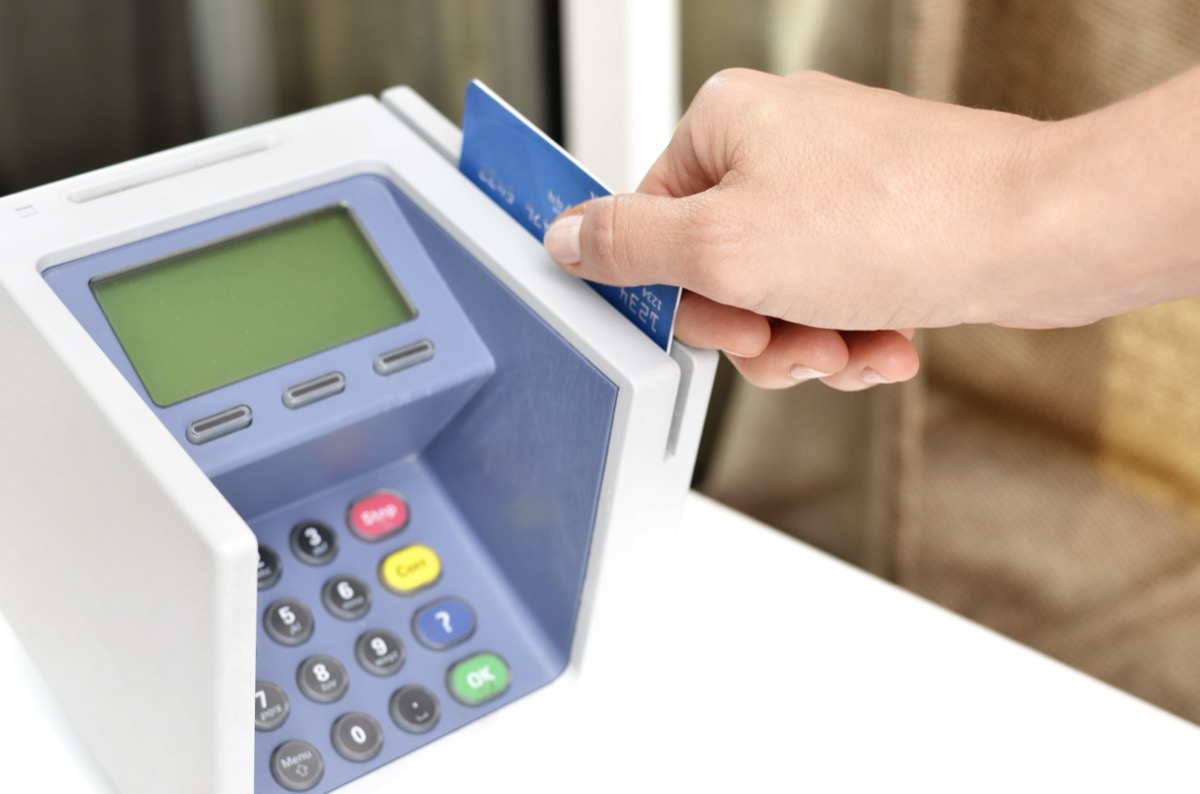 A close-up of a hand inserting a credit card into a countertop payment terminal with a green display and keypad.