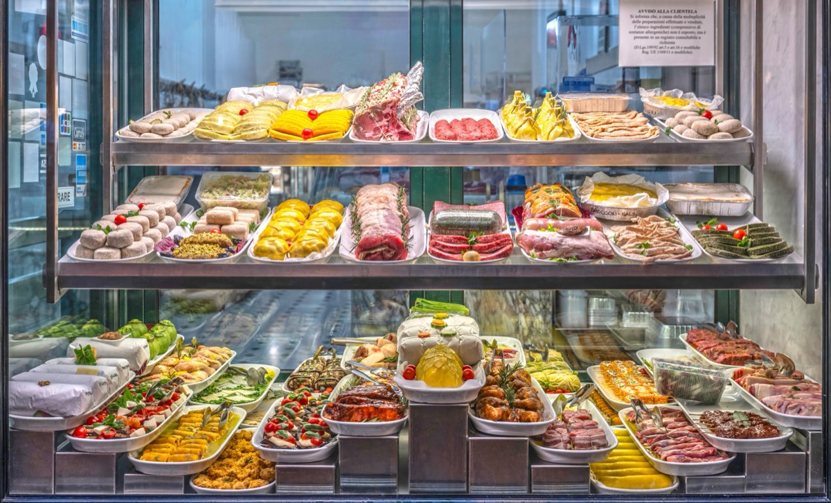 Glass deli counter filled with trays of cured meats, cheeses and prepared foods