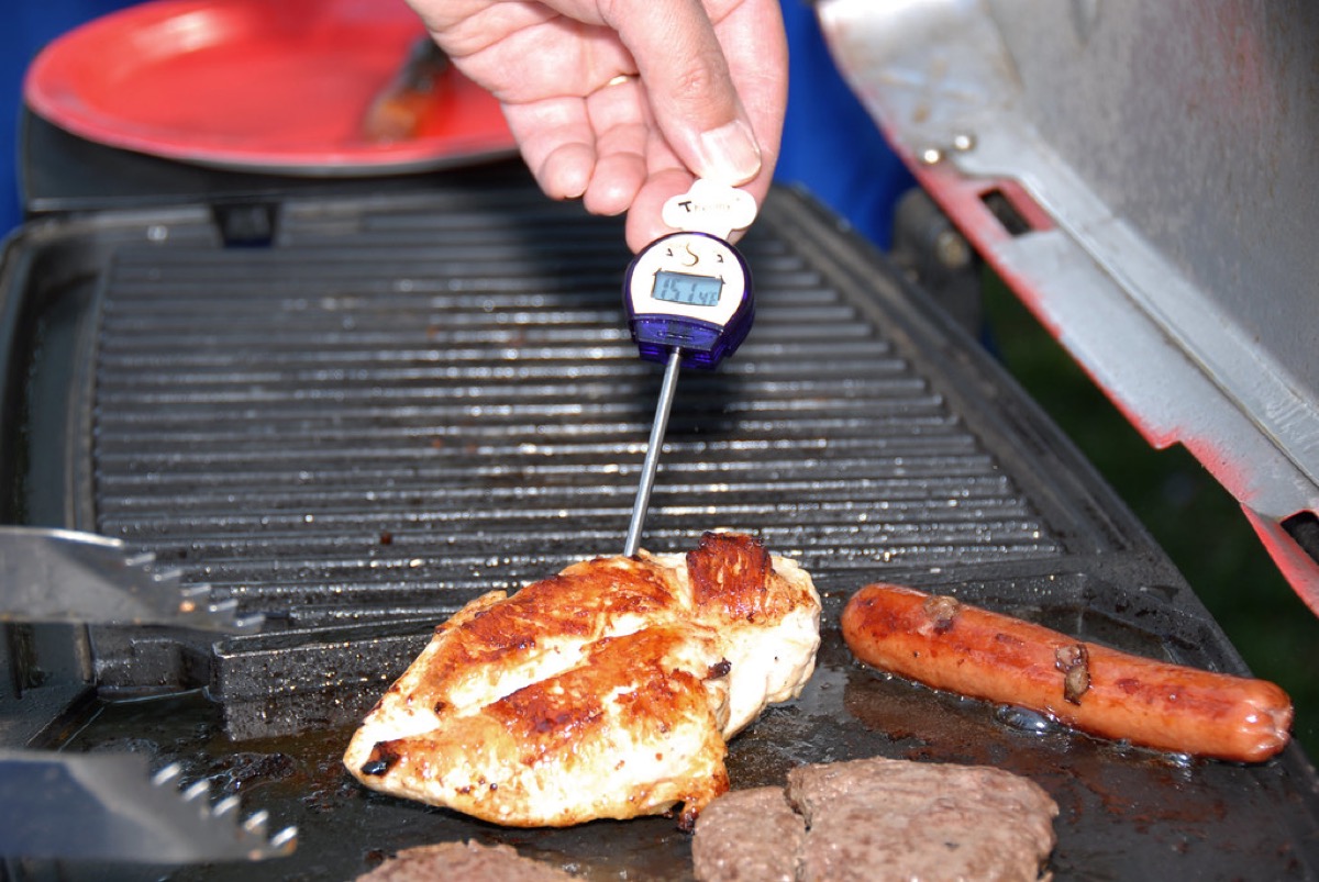 A digital probe thermometer inserted into a chicken breast on a grill to check its internal temperature