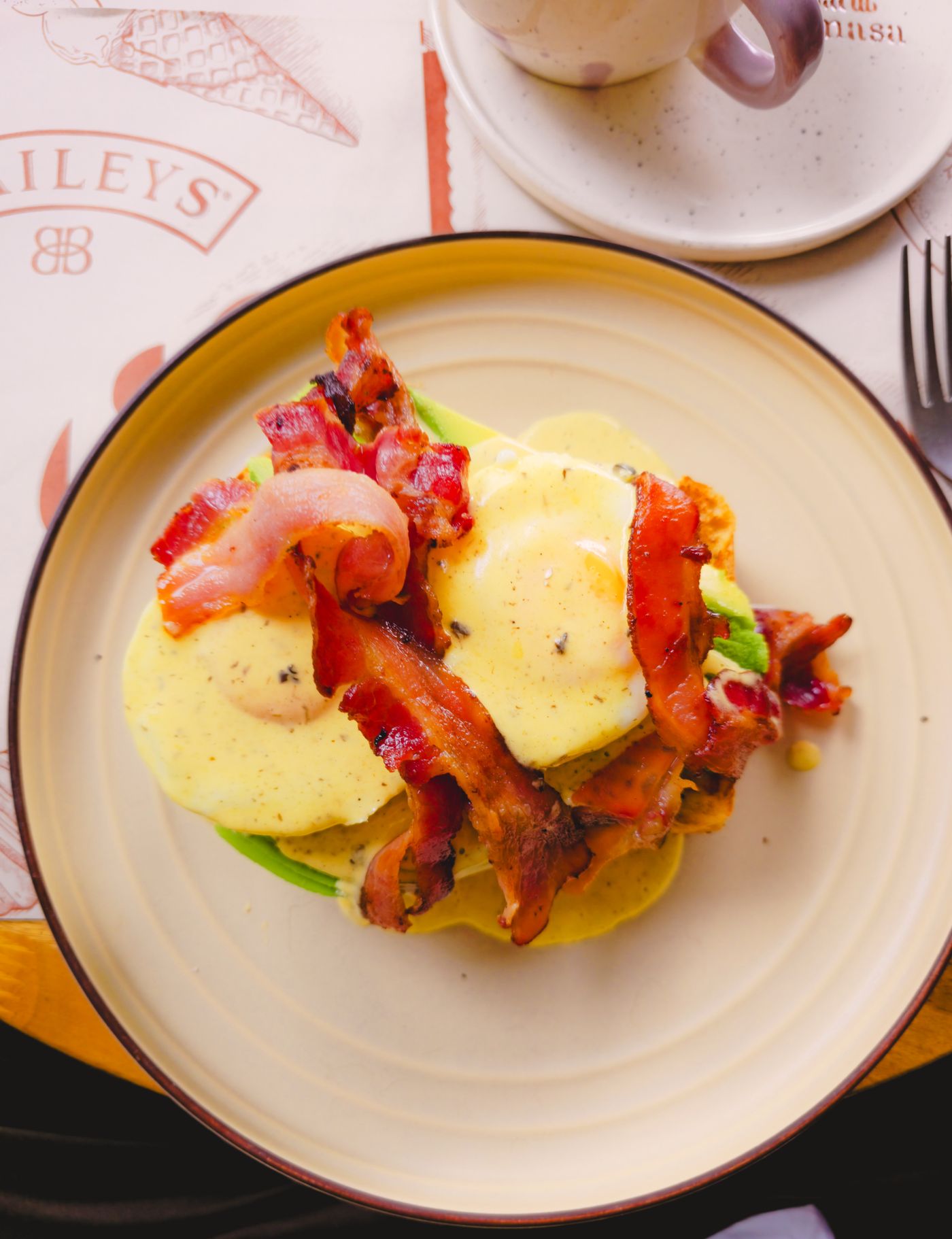 Overhead shot of eggs benedict topped with hollandaise sauce and crispy bacon on a plate