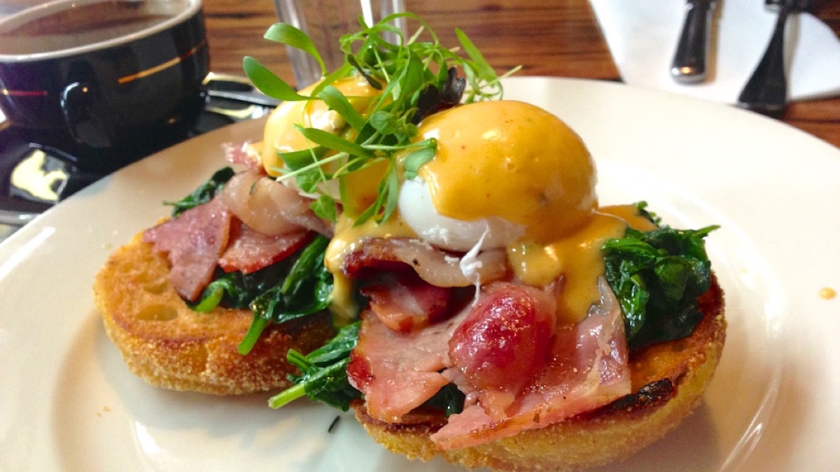 Eggs benedict on toasted muffins with bacon, wilted spinach, hollandaise and pea shoots, with coffee alongside
