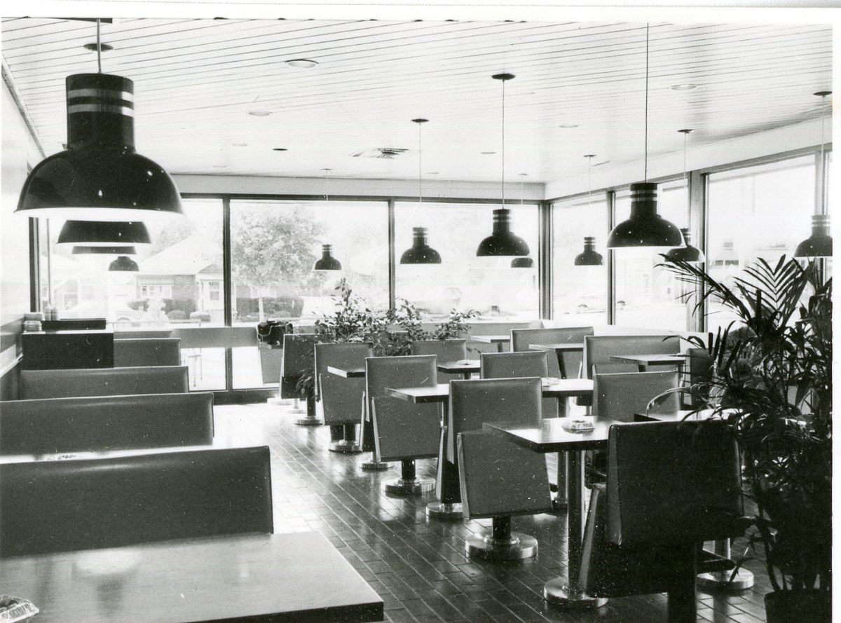 A vacant restaurant dining room with rows of empty booths and tables under pendant lights and large windows.