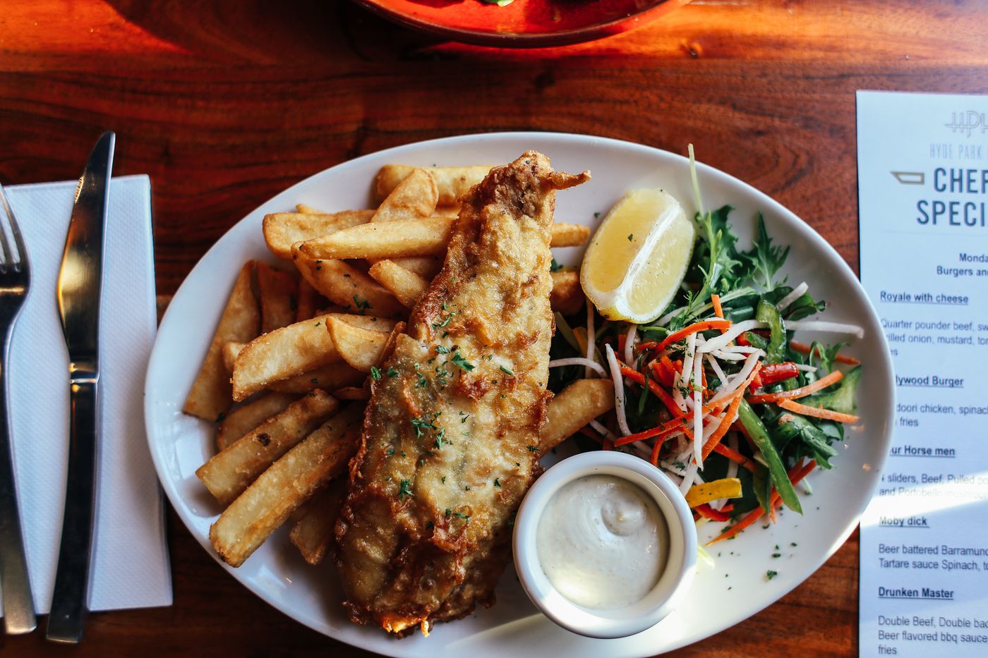 Crispy battered fish with thick-cut chips, fresh salad, lemon and tartare sauce on a plate