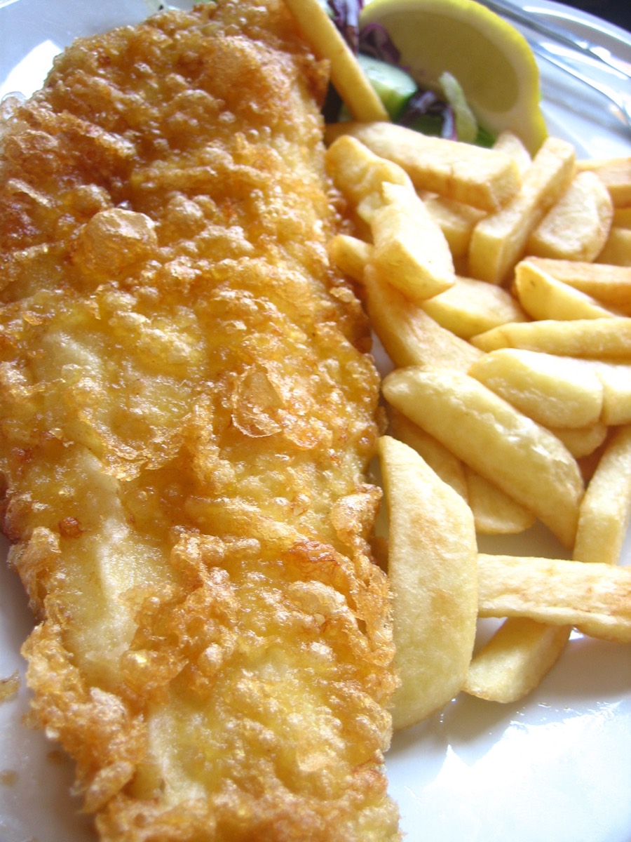 Close-up of golden beer-battered fish next to crispy chips, a lemon wedge and side salad on a white plate