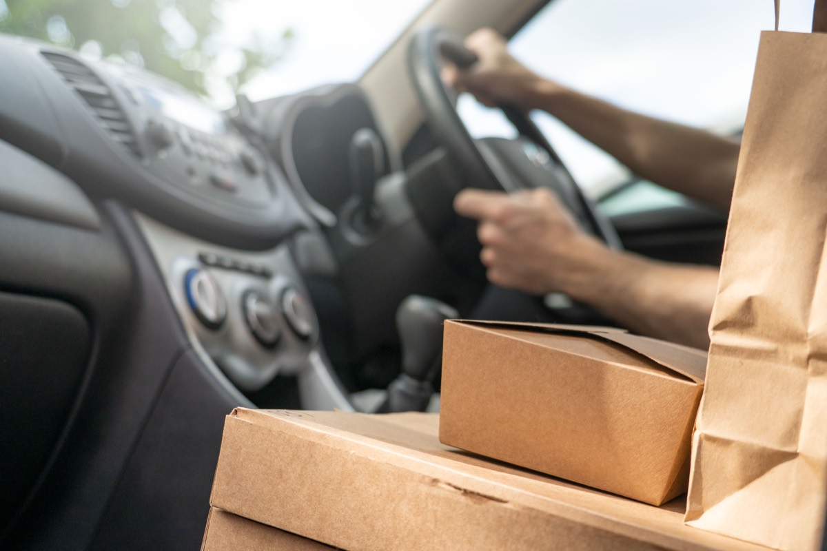 Kraft paper delivery bags and boxes stacked in a car while a driver holds the steering wheel