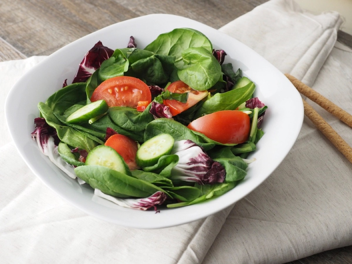 A white bowl of fresh spinach and radicchio salad with cherry tomatoes and cucumber, with breadsticks alongside