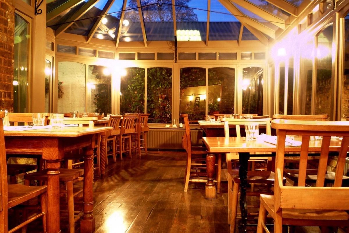 Evening view of a pub conservatory dining room with wooden tables, chairs, and warm lighting