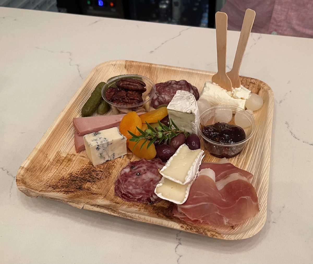 A wooden grazing board with prosciutto, salami, brie, blue cheese, olives, pickles, dried apricots and jam
