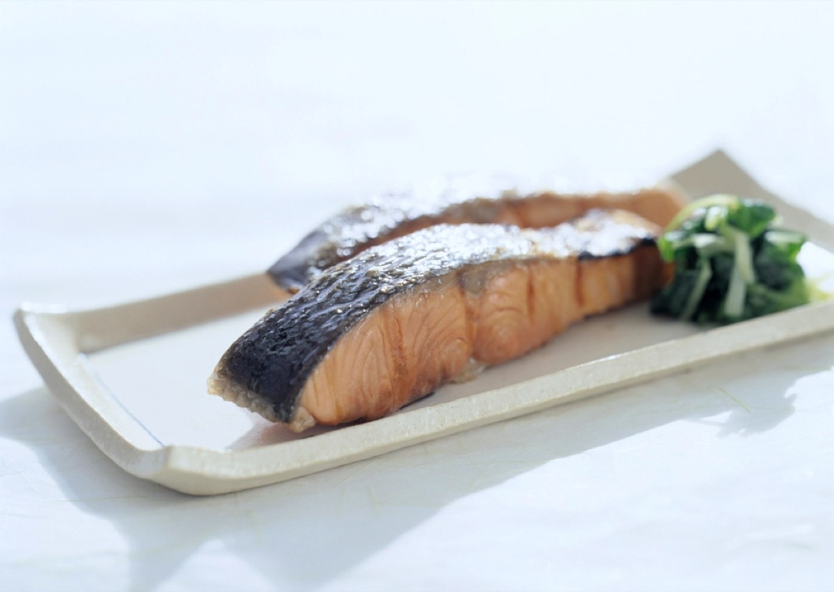 A grilled salmon fillet with crisp skin served with sauteed greens on a rectangular plate