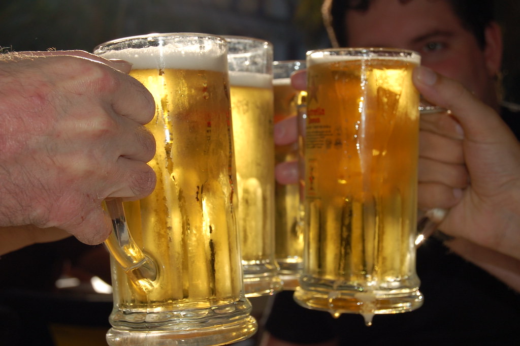 Two people clinking together frothy beer mugs in a toast at a bar