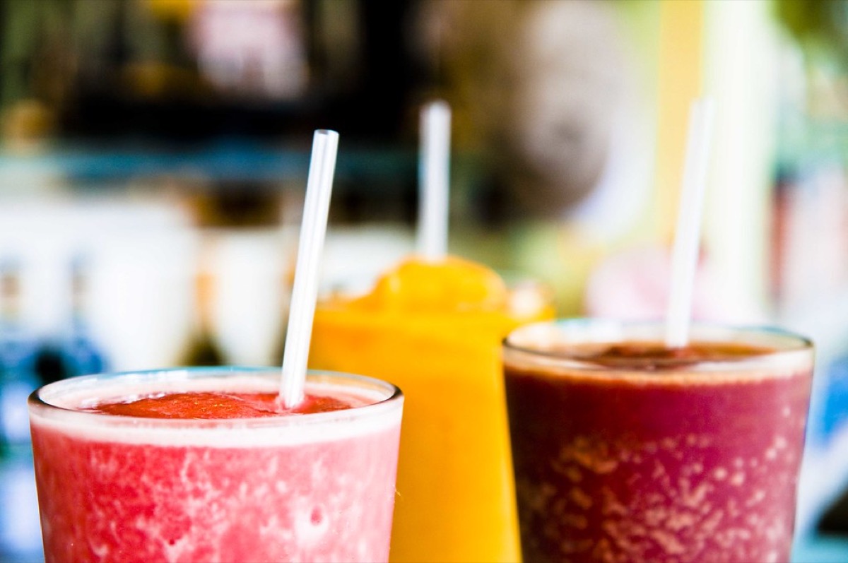 Three colourful blended smoothies with straws lined up on a juice bar counter
