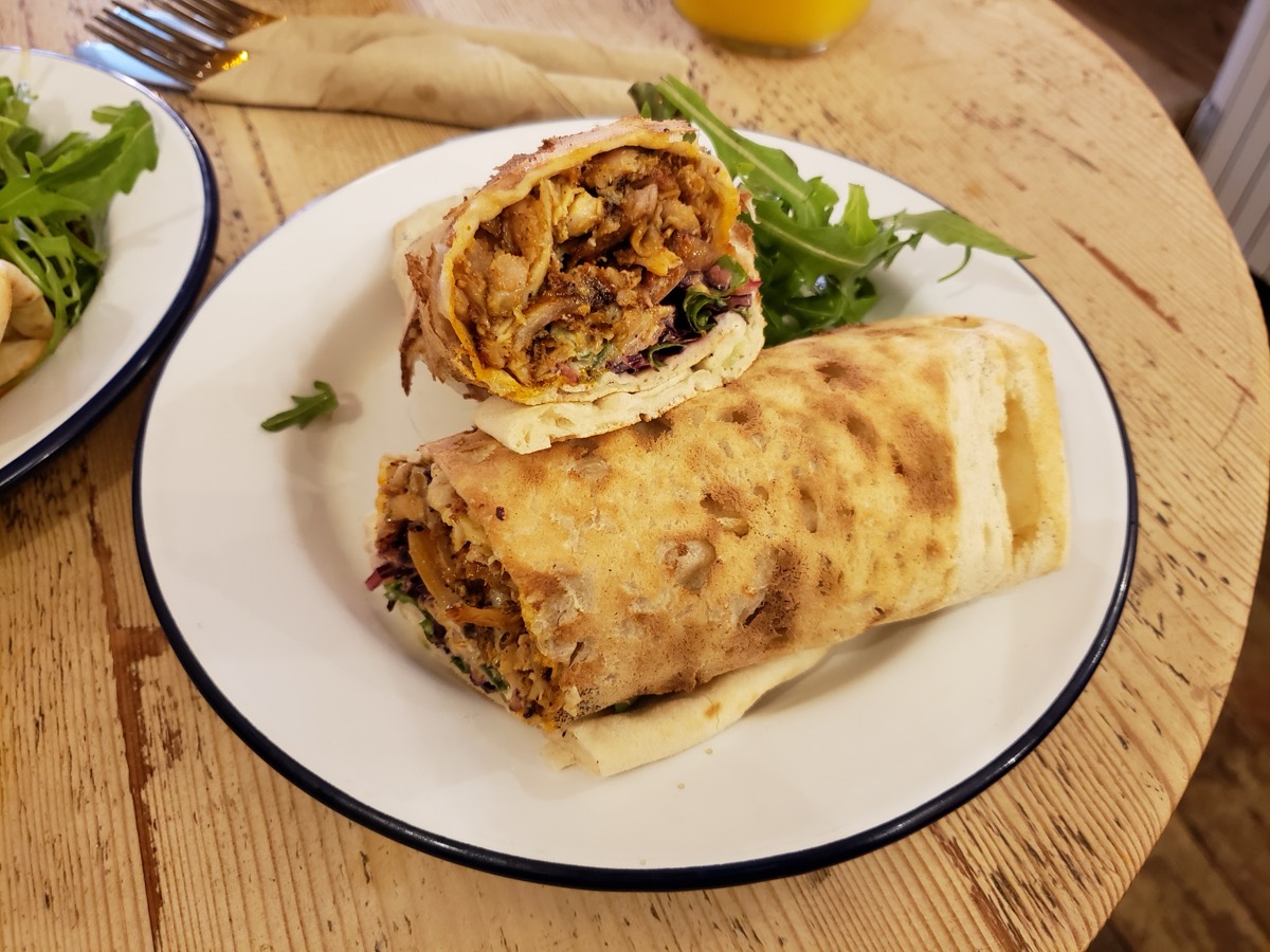 A chicken shawarma wrap cut in half and served on a plate with arugula salad on a wooden table