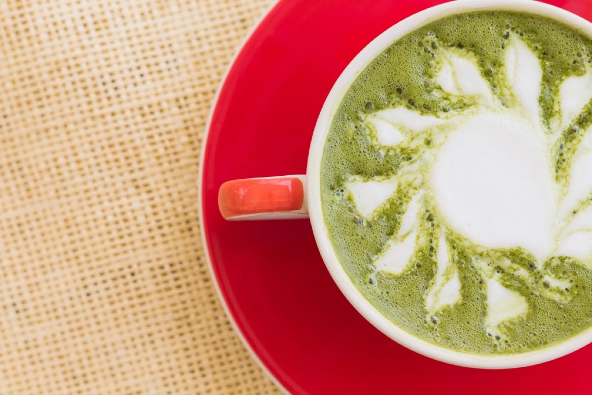 An overhead matcha green tea latte with a milk leaf pattern in a white cup on a red saucer