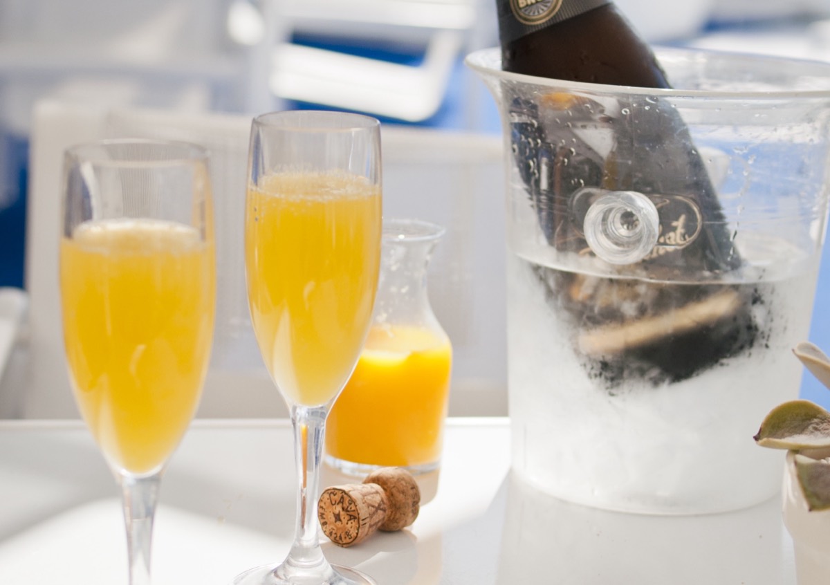 Two mimosa cocktails in champagne flutes beside a chilled bottle in an ice bucket on a bright table