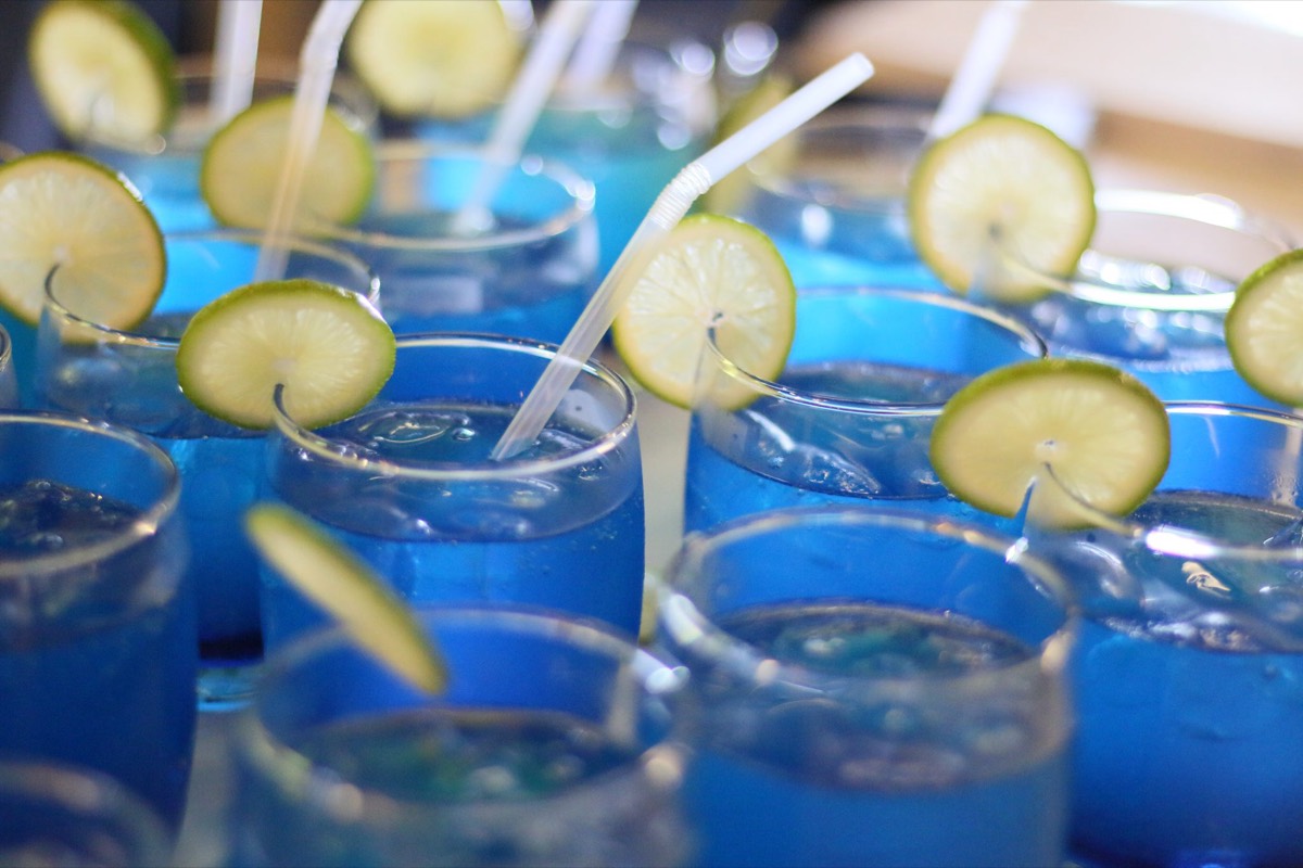 A row of bright blue mocktails in stemless glasses, each garnished with a lime slice and a white straw
