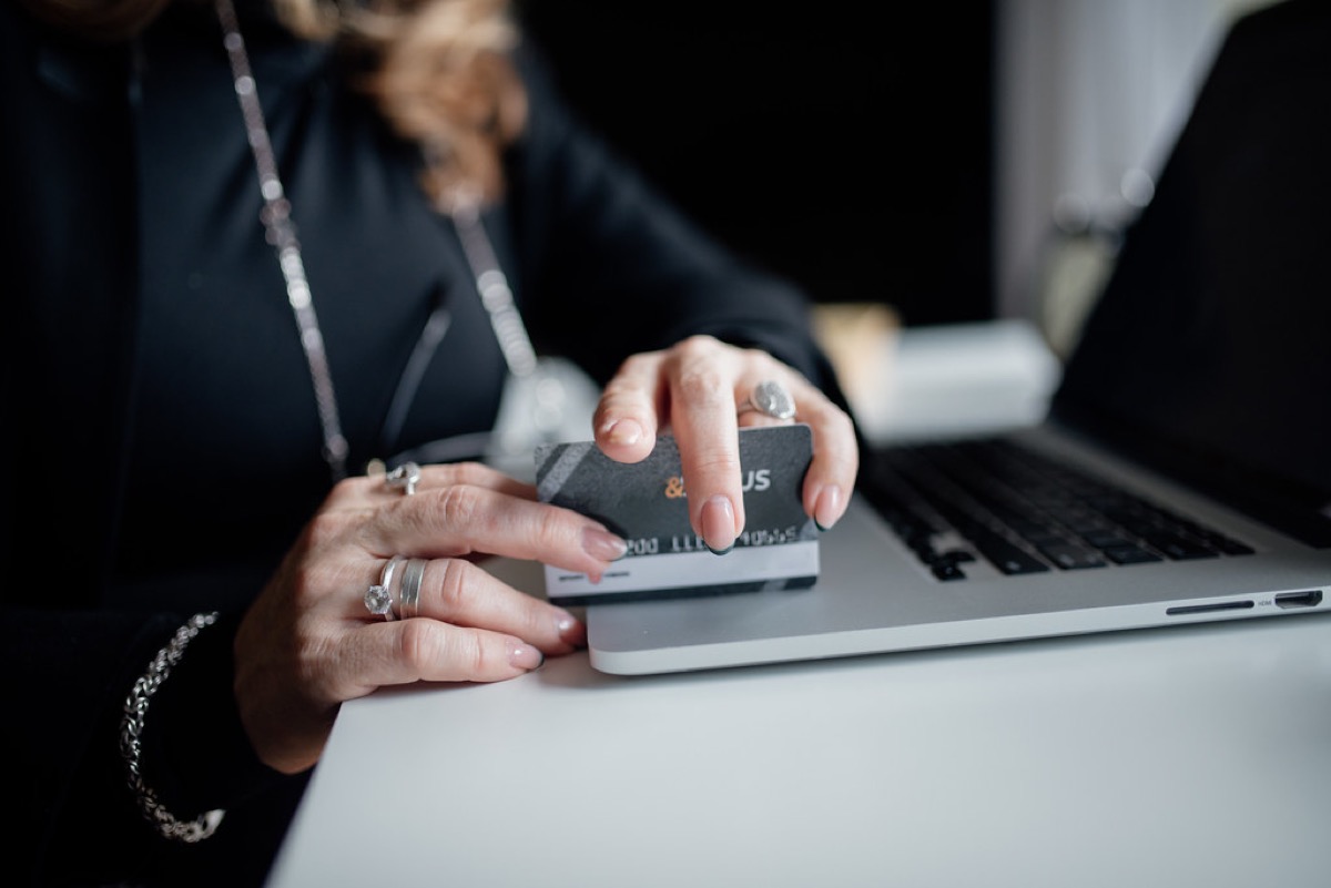 A person's hands hold a credit card above an open laptop keyboard while entering the card details to complete an online purchase.
