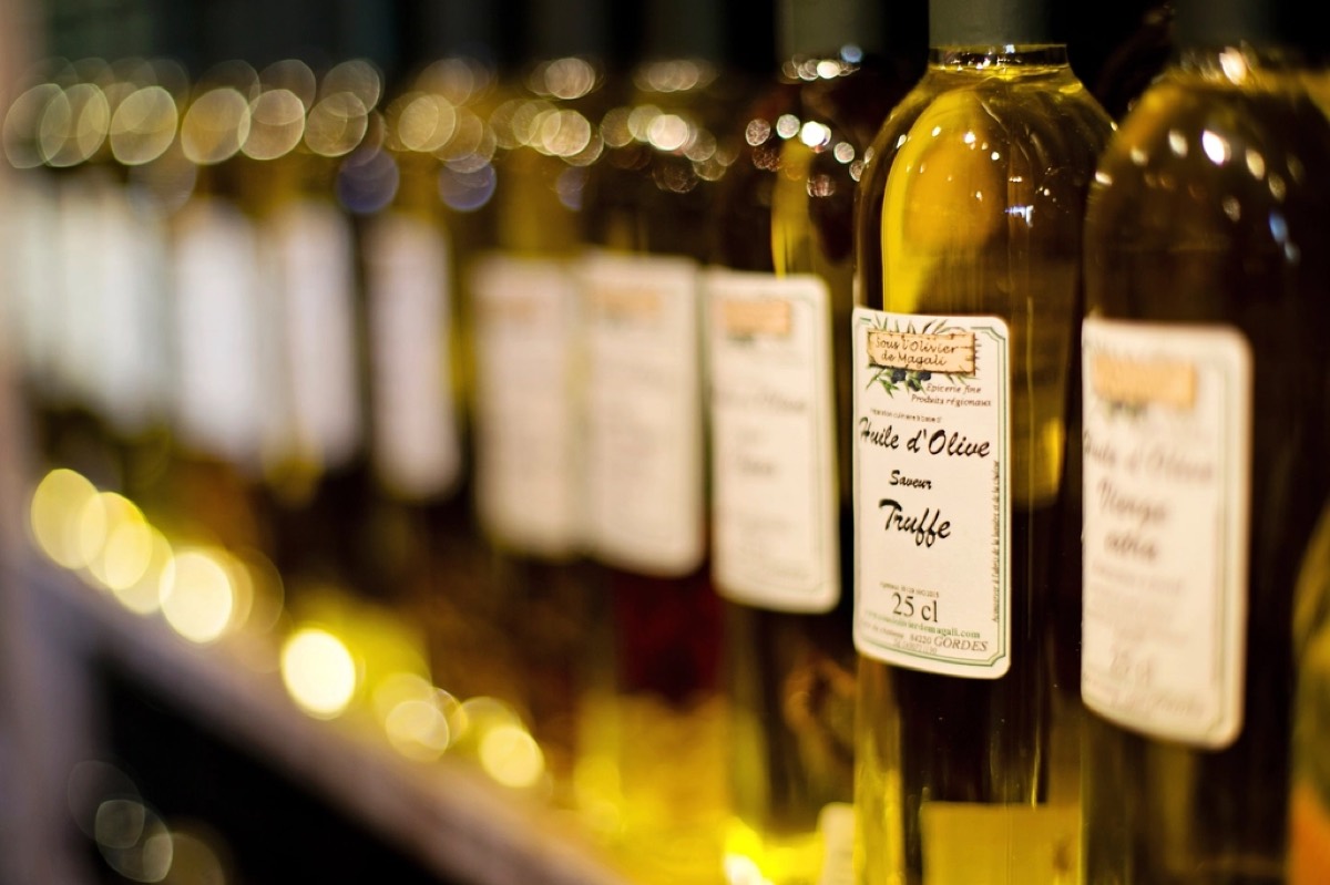 A row of labelled olive oil bottles lined up on a shelf with warm bokeh lights in the background