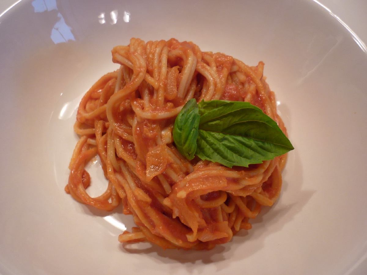 Overhead view of a twirled pasta al pomodoro dish topped with a fresh basil leaf in a white bowl.