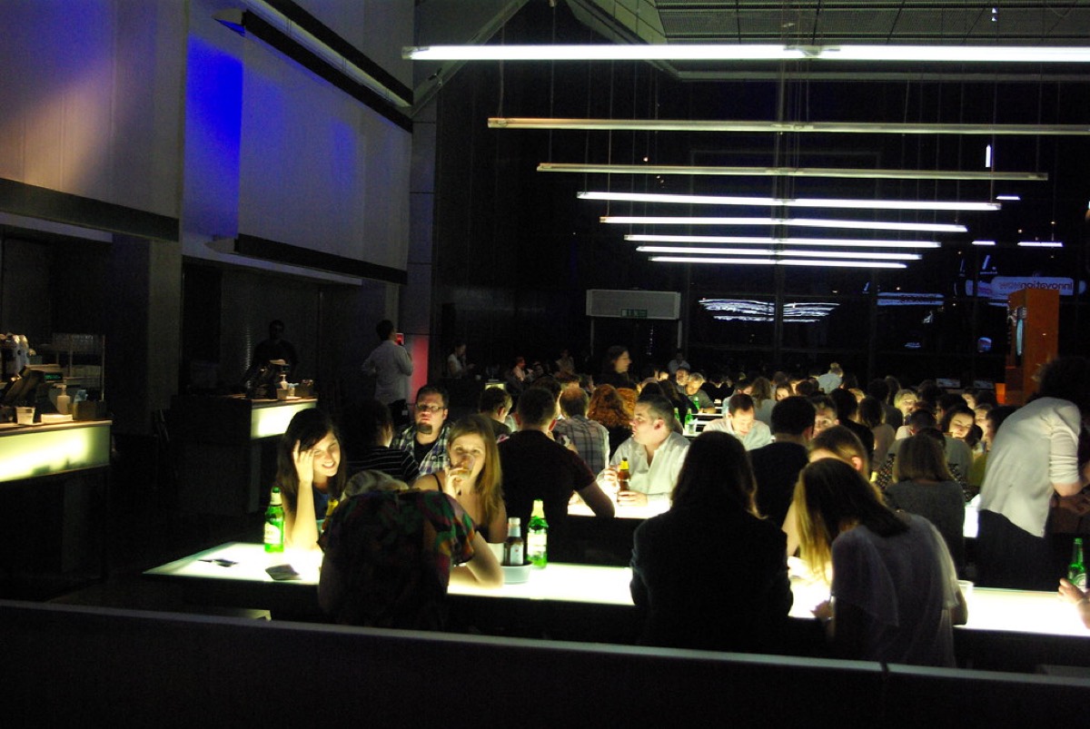 A large crowd seated at long illuminated tables taking part in a busy evening pub quiz