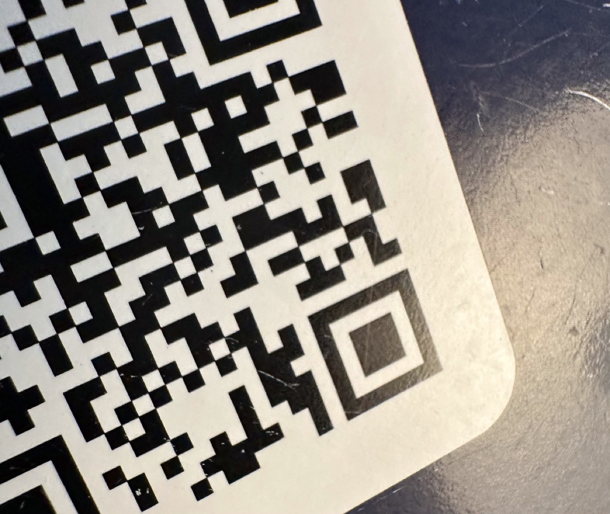 A close up macro photo of a black and white QR code sticker on a worn tabletop surface.