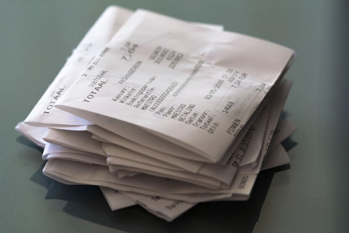 A folded stack of printed paper till receipts sitting on a plain grey tabletop.