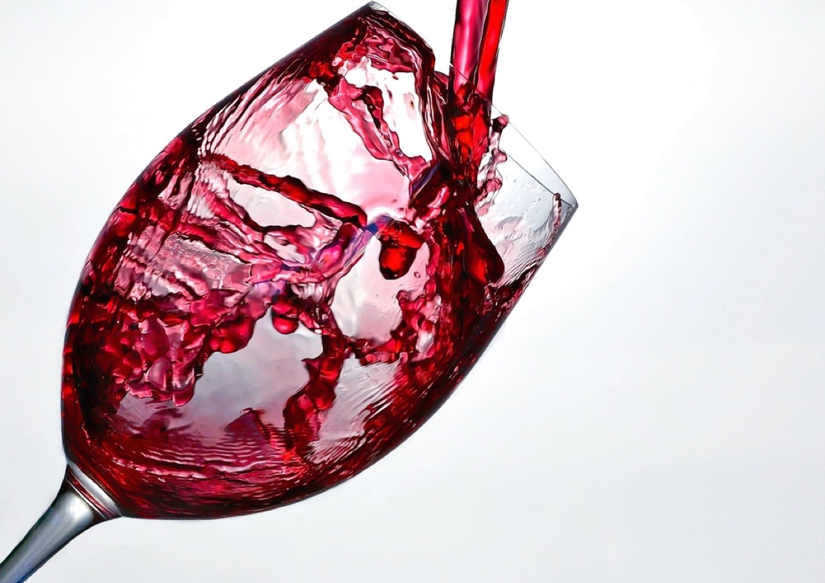 Red wine pouring and splashing into a wine glass against a plain white background