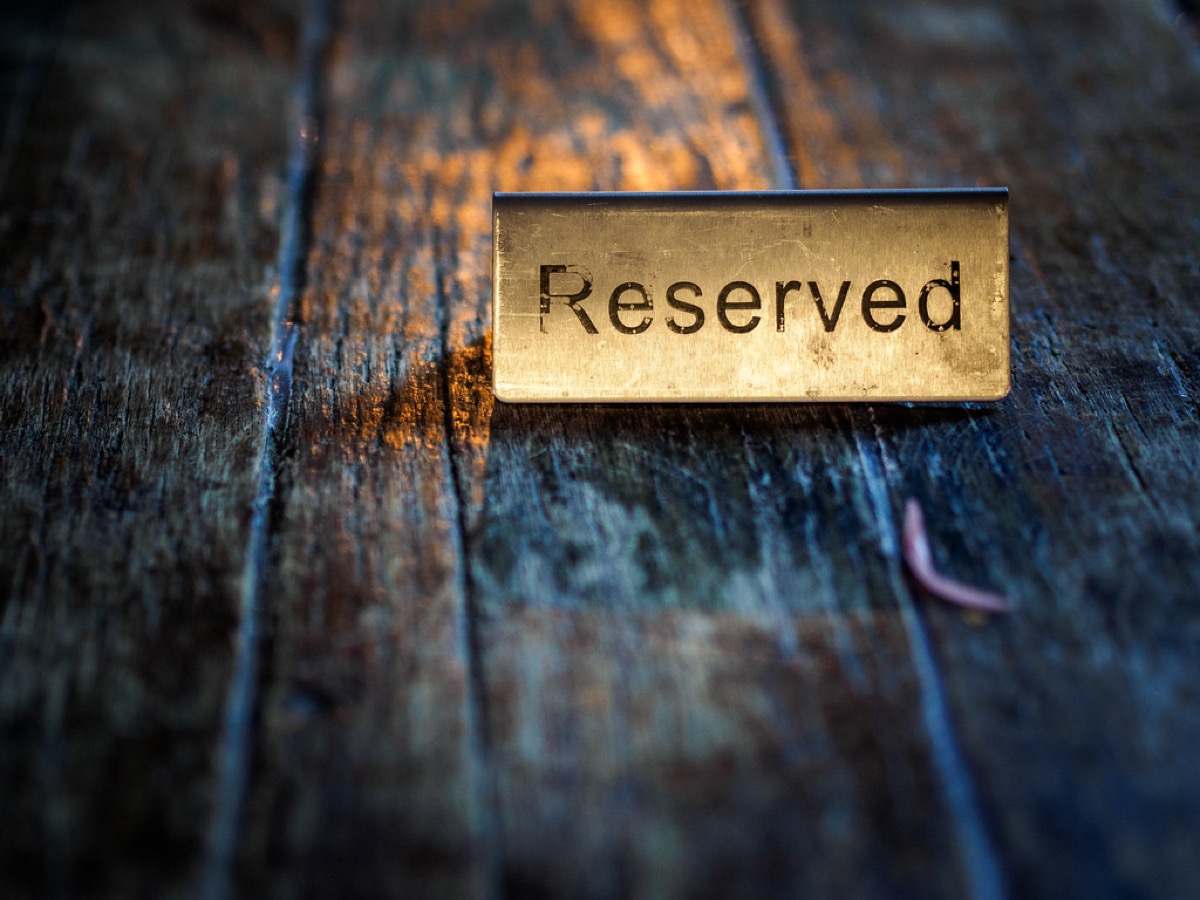 A brass Reserved table sign resting on a weathered wooden restaurant table.