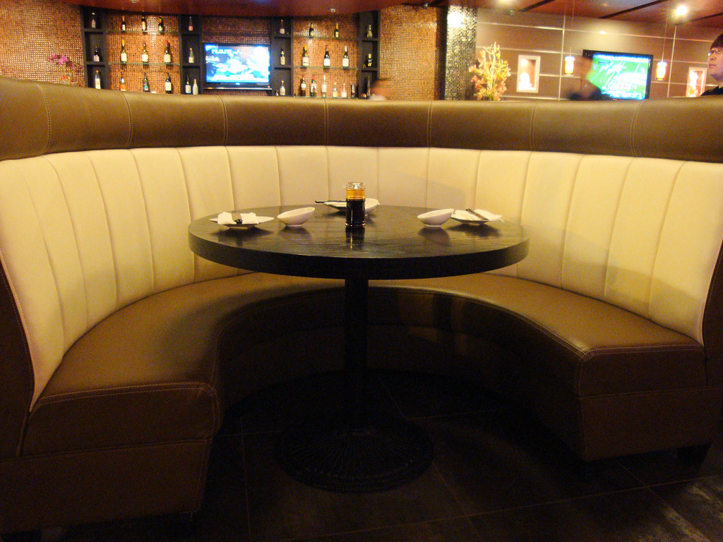 A curved cream and brown leather restaurant booth wrapped around a round black table, set for dining