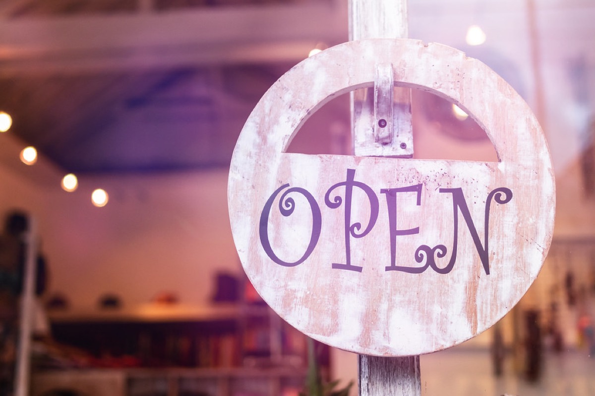 A rustic wooden OPEN sign hanging in a cafe window with warm string lights blurred in the background.