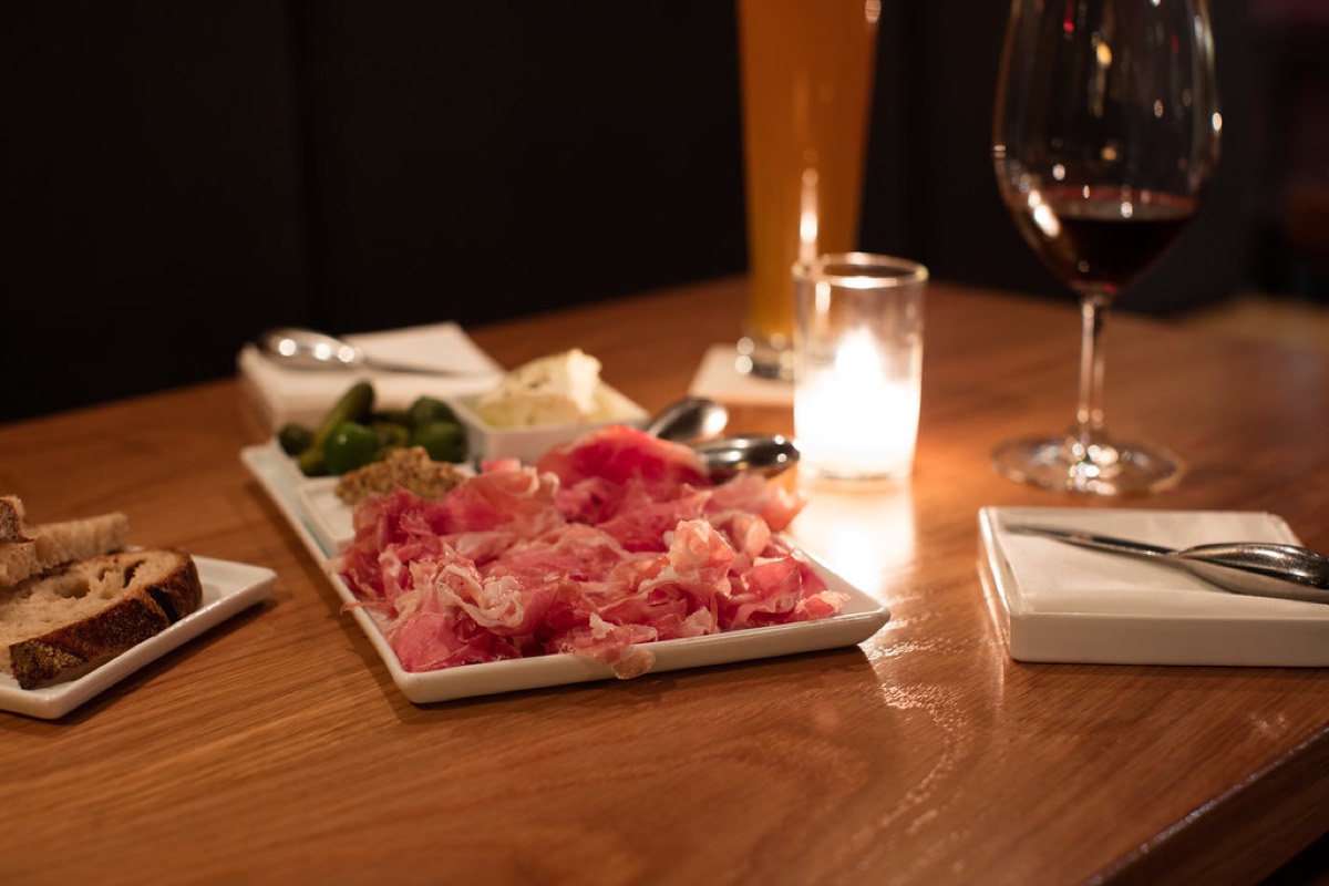 A candlelit restaurant table with a charcuterie plate, sliced bread, and a glass of red wine