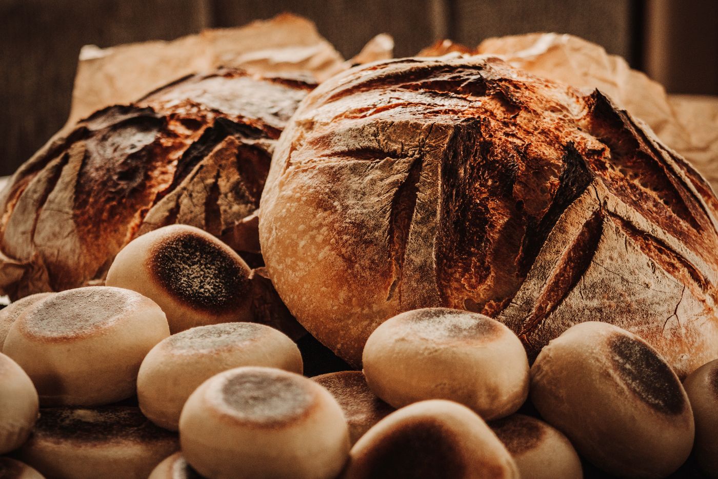 Close-up of two crusty rustic sourdough loaves with English muffins on a wooden surface