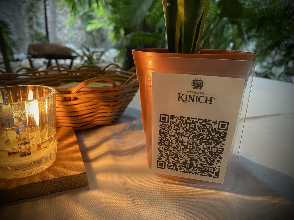 A printed QR code menu card standing on a candlelit restaurant table with a bread basket
