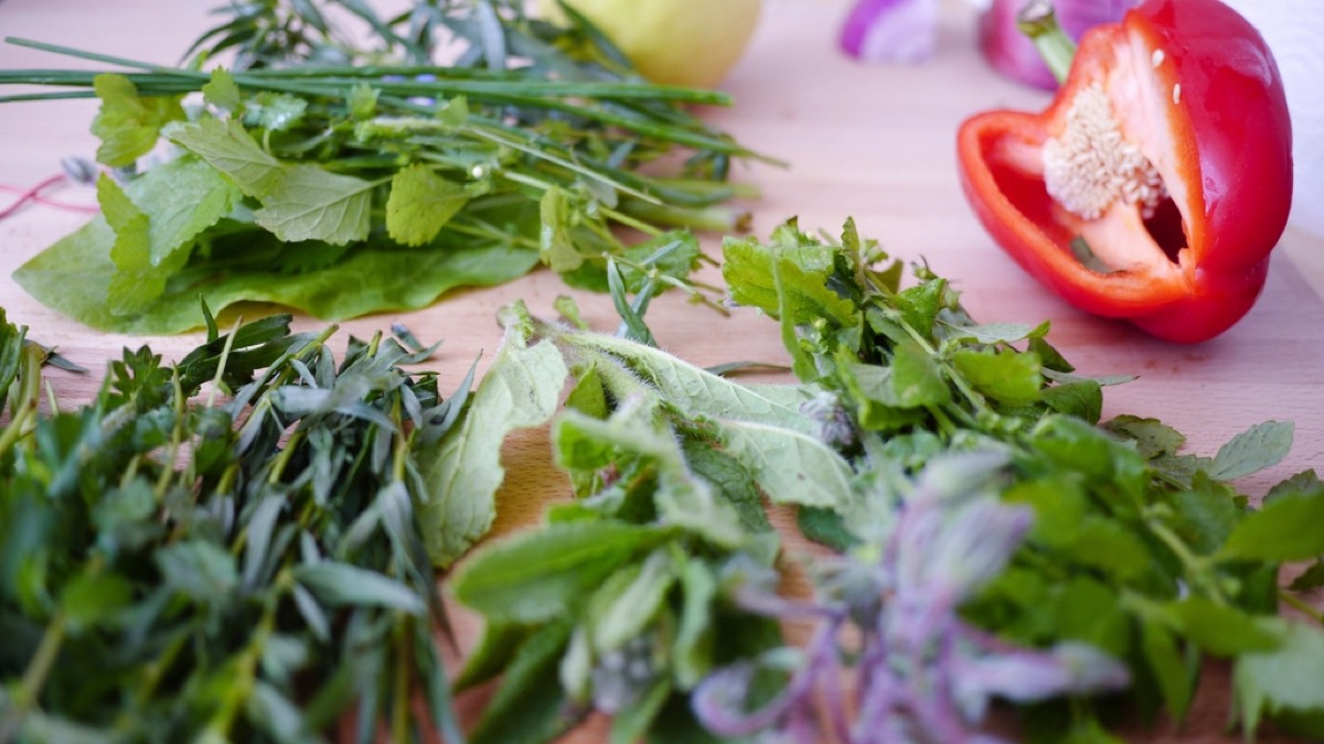 Fresh herbs and a halved red pepper arranged on a wooden cutting board