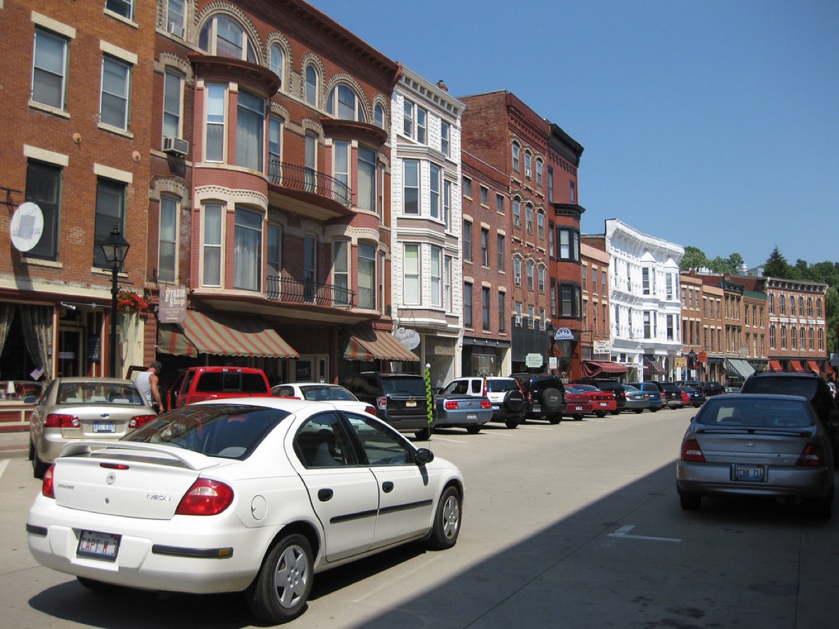 A sunny main street lined with independently owned shops in historic brick buildings, with cars parked along the kerb.
