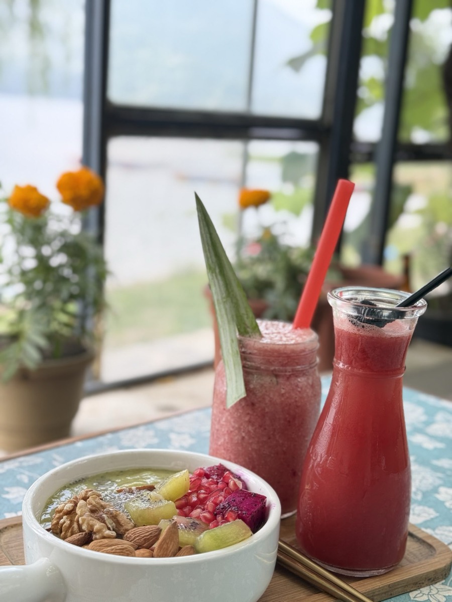 A smoothie bowl topped with walnuts, almonds, kiwi and pomegranate next to a pink smoothie and a bottle of red juice