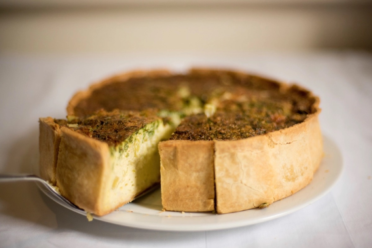 A whole spinach quiche with a golden pastry crust, one slice being lifted out on a server