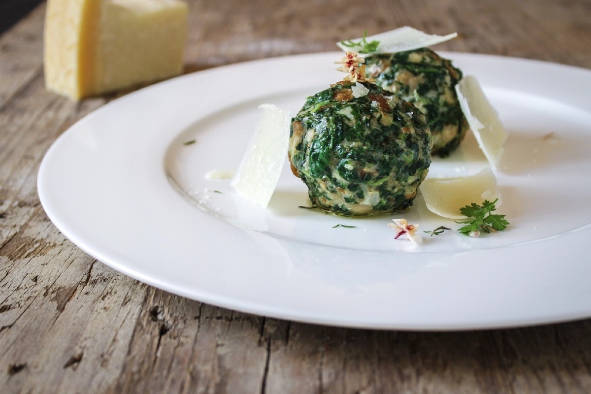Two spinach and ricotta dumplings on a white plate with shaved parmesan and micro herbs