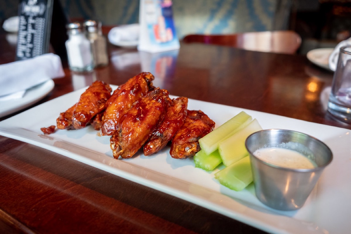 A plate of glazed chicken wings with celery sticks and ranch dip on a bar table